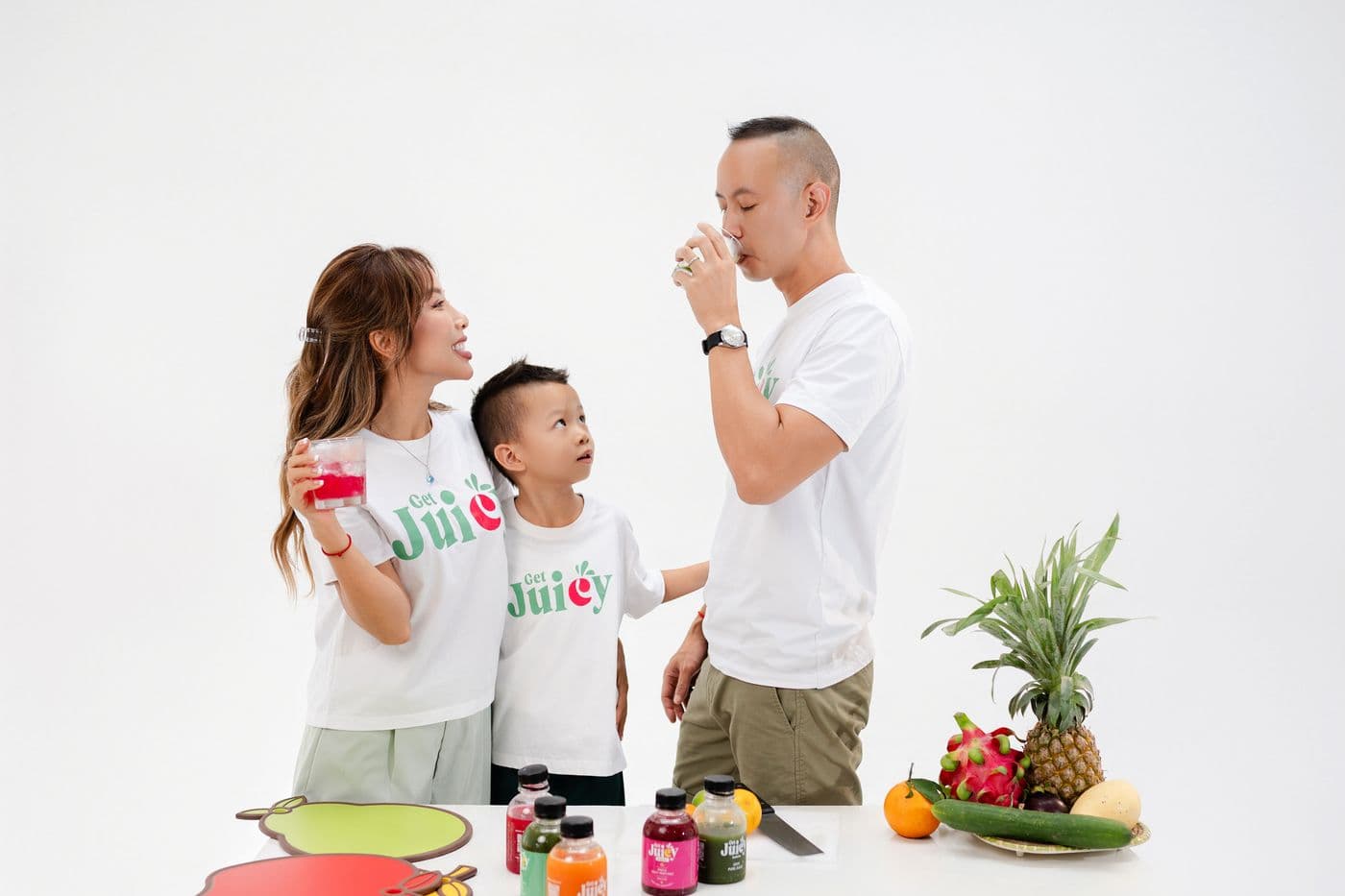 Linh đang uống nước ép, Mylan và Sky nhìn theo, trên quầy là các chai nước và trái cây tươi