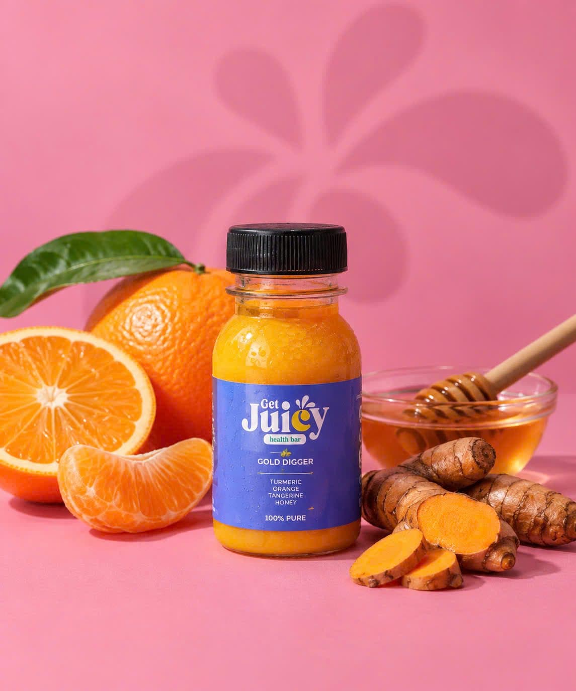 A Gold Digger shot next to oranges, honey and turmeric root