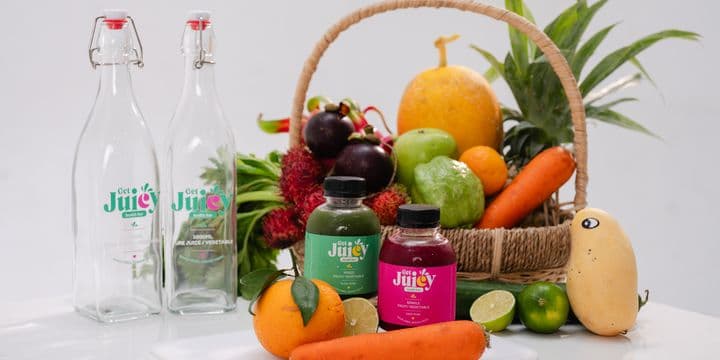 A basket of fruit and vegetables next to Juicy bottles